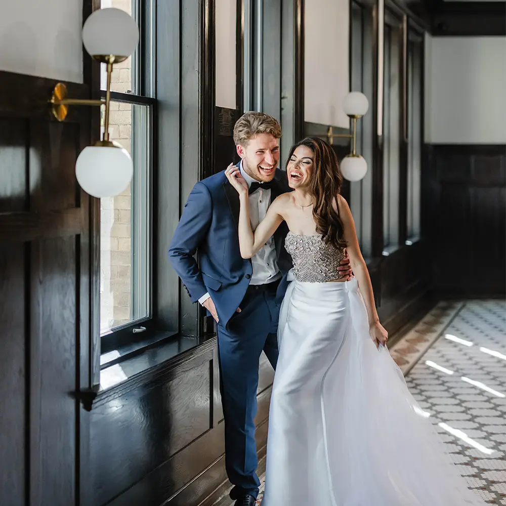groom and bride pose in front of window
